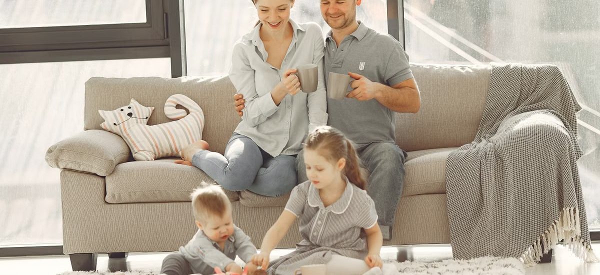 Cheerful family wearing casual clothes sitting in living room while playing and drinking tea during weekend at home in morning