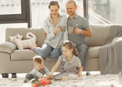 Cheerful family wearing casual clothes sitting in living room while playing and drinking tea during weekend at home in morning