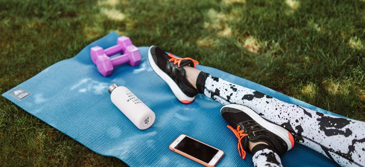 Focused workout setup outdoors with mat, dumbbells, phone, and water bottle.